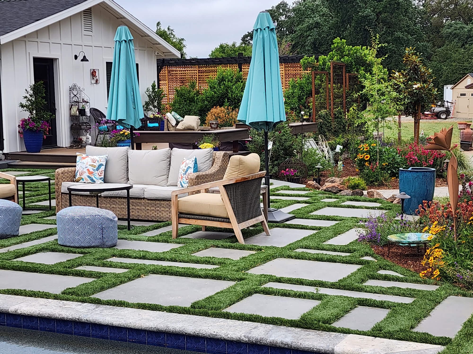 Poolside outdoor living area with a turf-and-paver checkerboard patio and market umbrellas