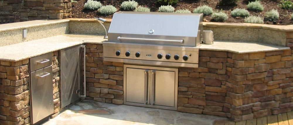 Stacked-stone outdoor kitchen island with a built-in stainless grill and a curved seat wall