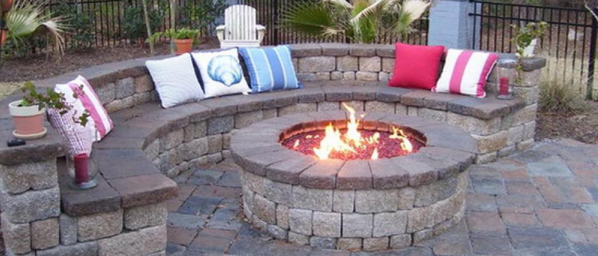 Paver fire pit ringed by a curved seat wall with cushions on a paver patio