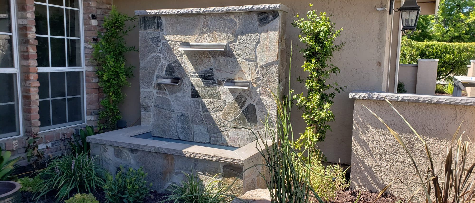 Stacked-stone water wall with stainless steel spouts spilling into a stone basin