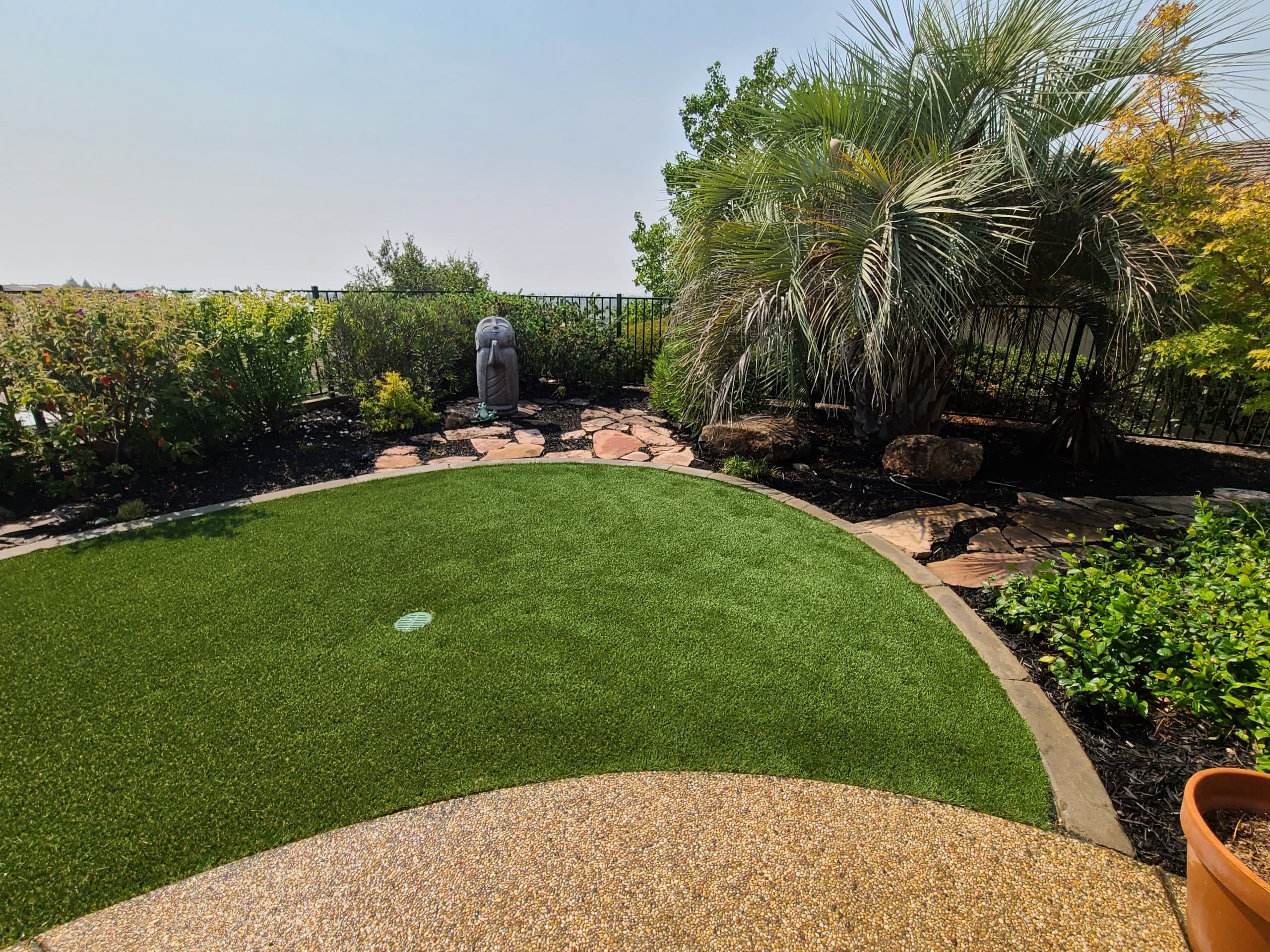 Circular artificial turf putting green bordered by flagstone and a pebble patio